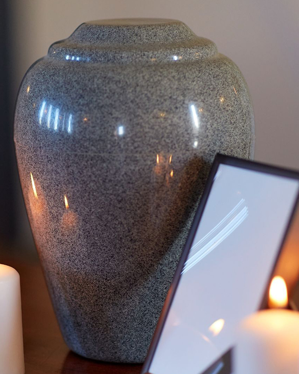 a granite urn on a table next to lit candles and a frame